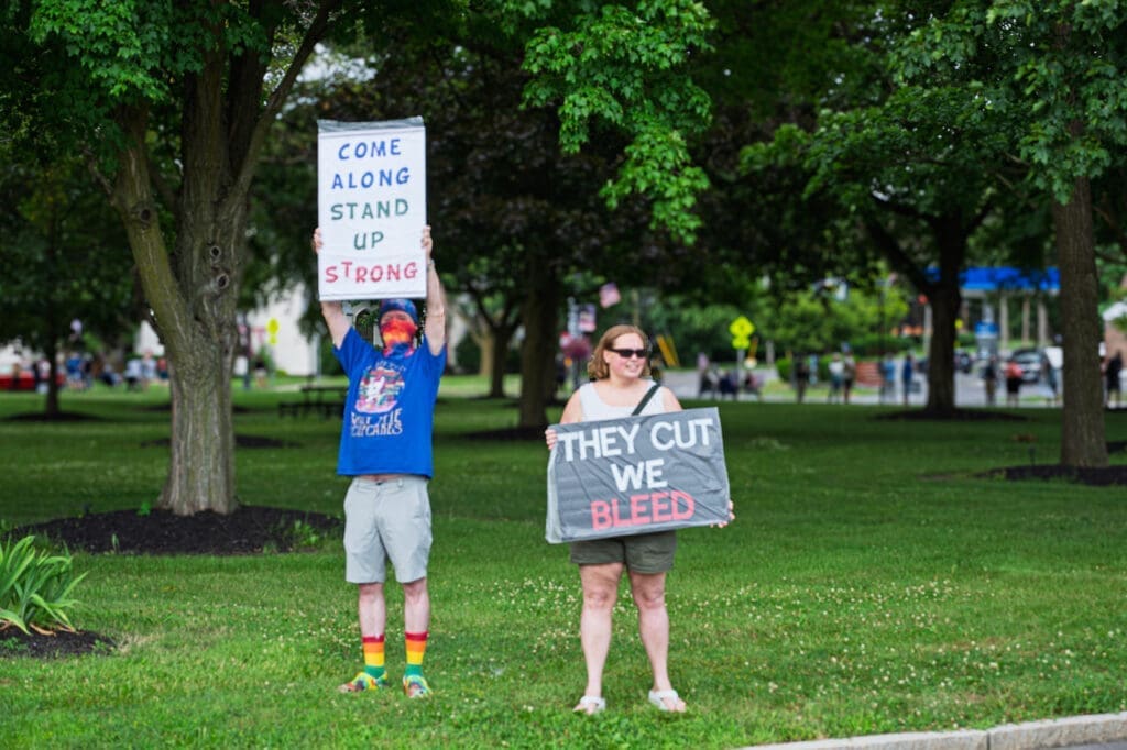 Two people holding protest signs in a park.