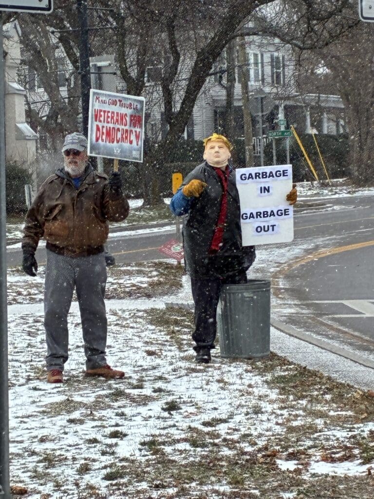 Two people holding protest signs in snowy street.