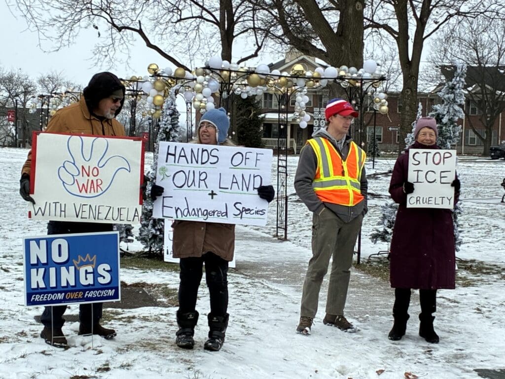 Protesters holding anti-war and environmental signs in snow.