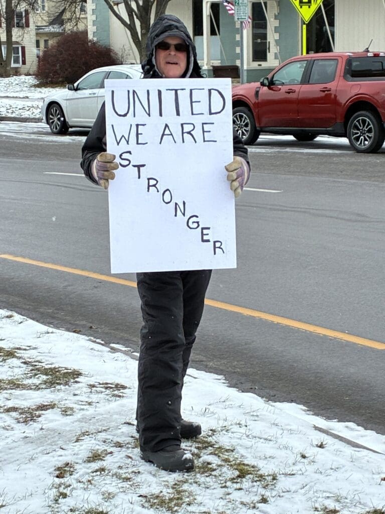 Person holding 'United We Are Stronger' sign in snow.
