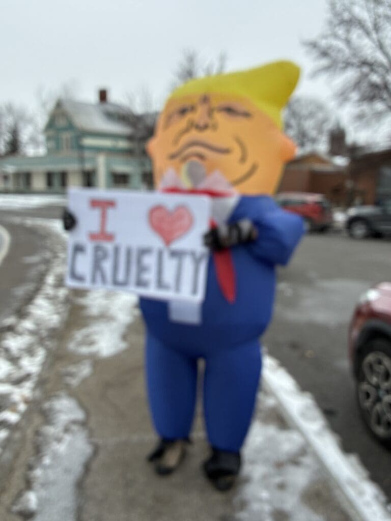 Inflatable costume holding sign in snowy street.