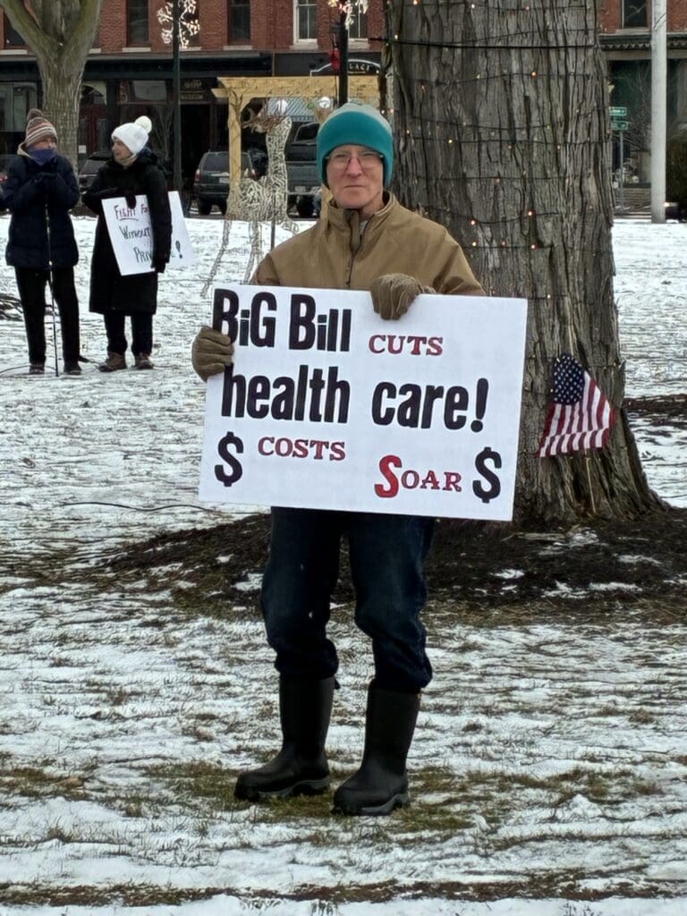 Protester holds healthcare bill sign in snowy park.