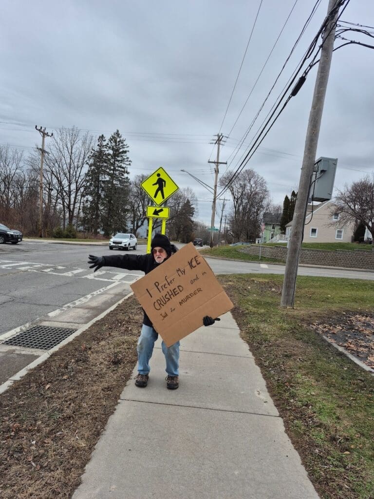 Person holding cardboard sign on sidewalk.
