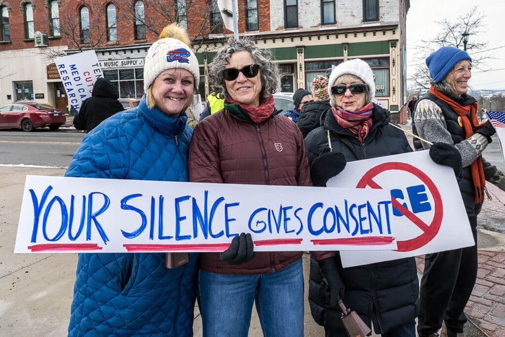 Women holding protest sign reading Your Silence Gives Consent