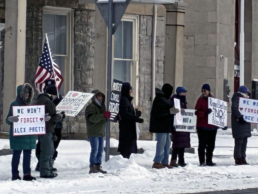 People holding signs in snowy protest with American flag.