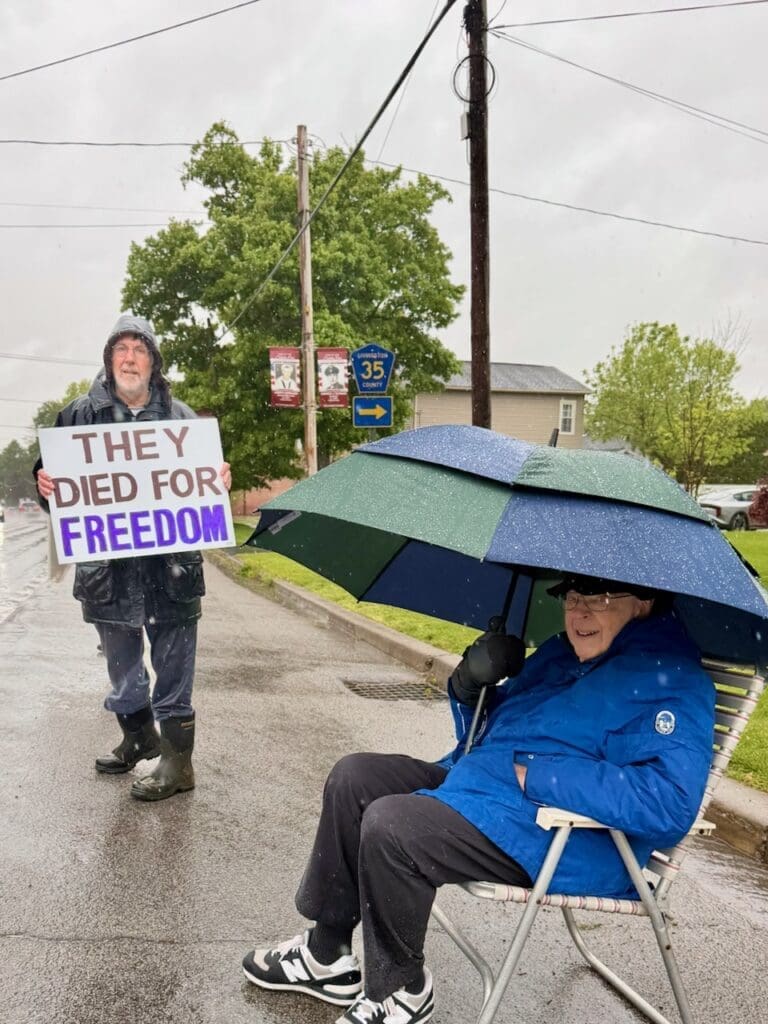 Man holding freedom sign in rain beside seated man.