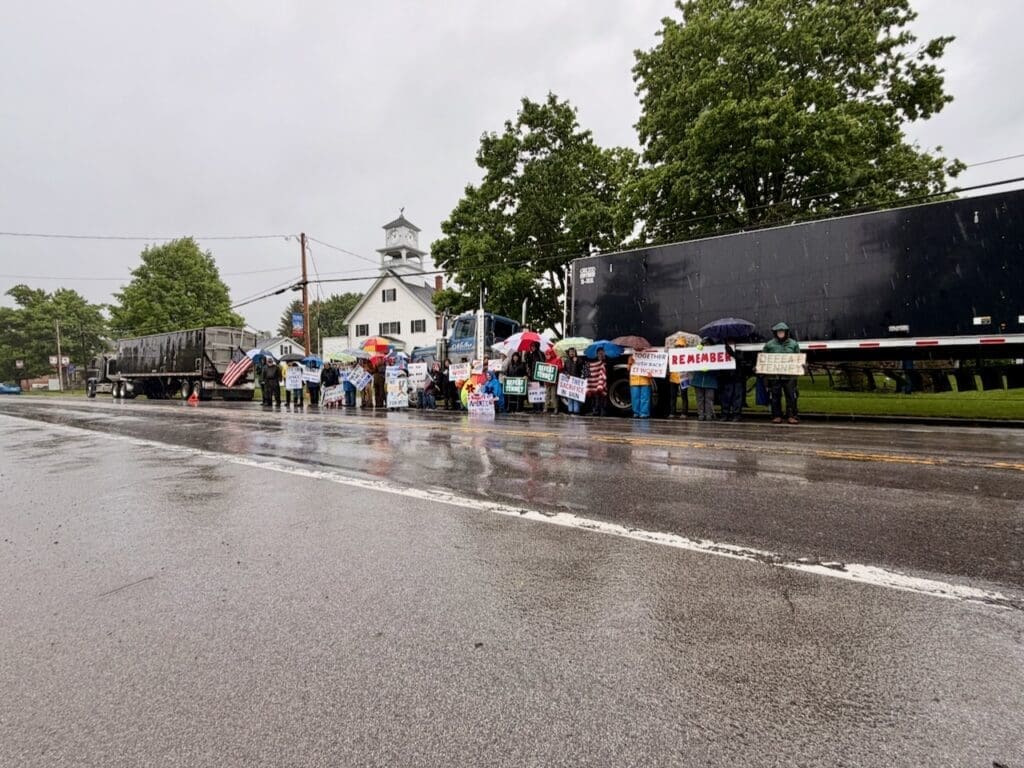 People holding protest signs in rain by roadside
