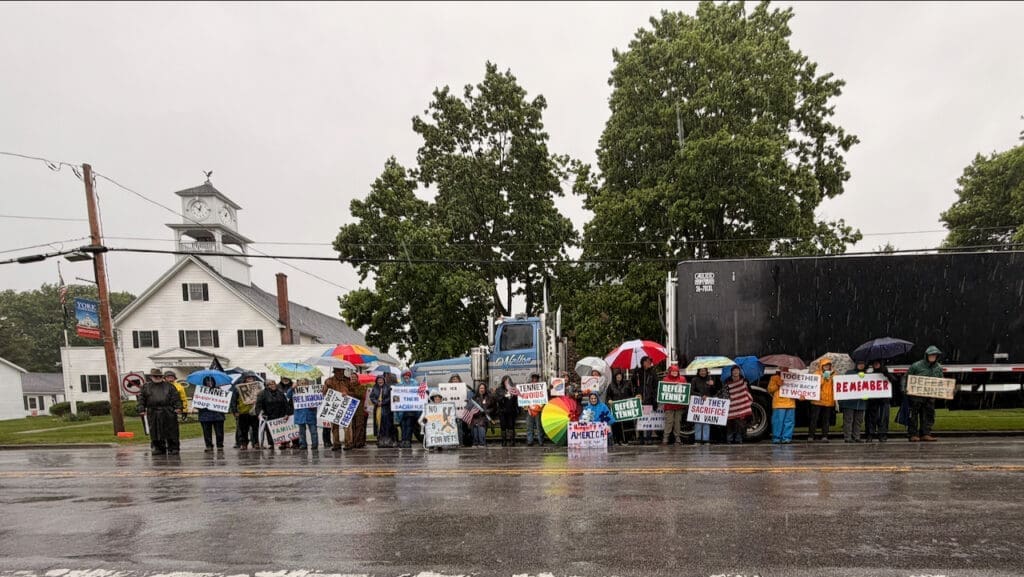 Protesters with umbrellas holding signs in rainy street