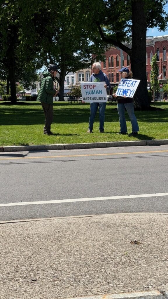 Protesters holding anti-warehouse and anti-Tenney signs.
