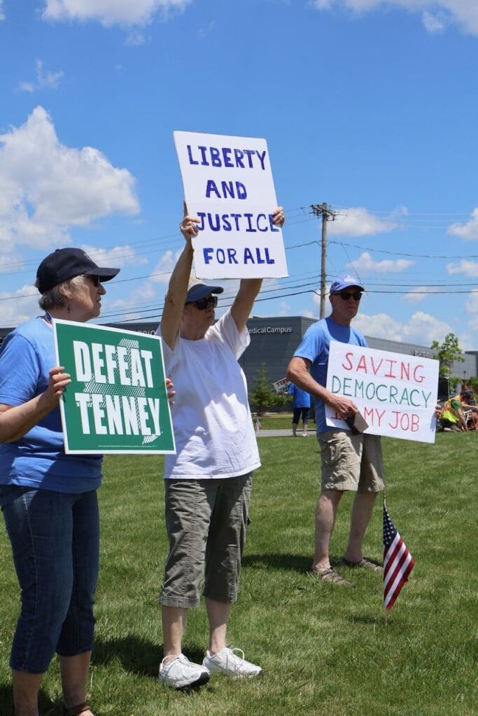 Protesters holding signs for liberty, democracy, and defeating Tenney