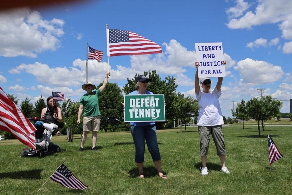 Protesters holding Defeat Tenney and Liberty Justice signs outdoors