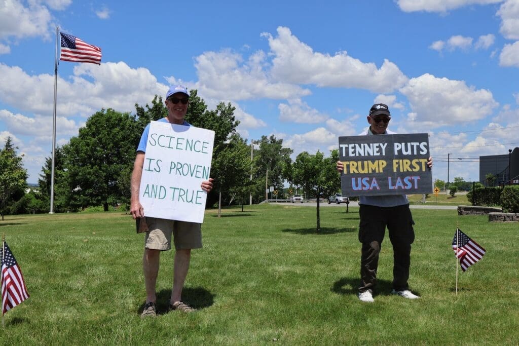 Two protesters holding political signs outdoors near American flags