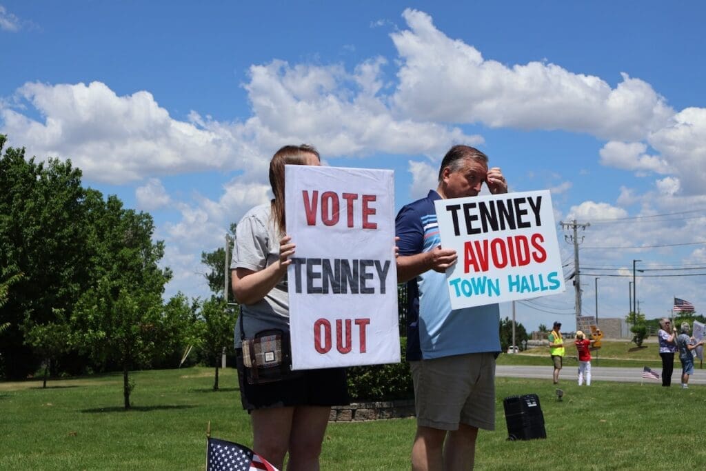 Protesters holding signs against Congresswoman Tenney outdoors
