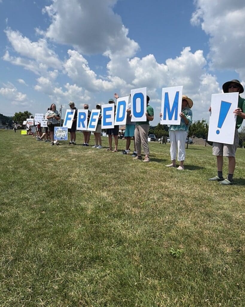 Protesters holding signs spelling FREEDOM on a grassy field