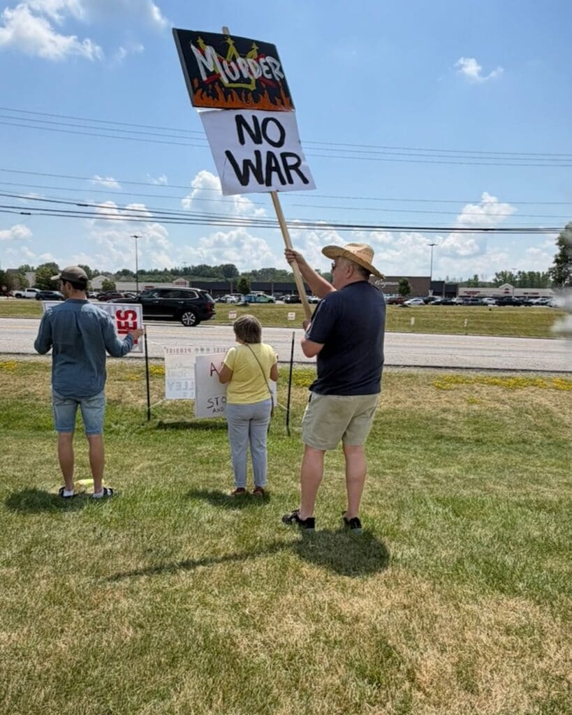 Protesters holding No War signs on roadside grass