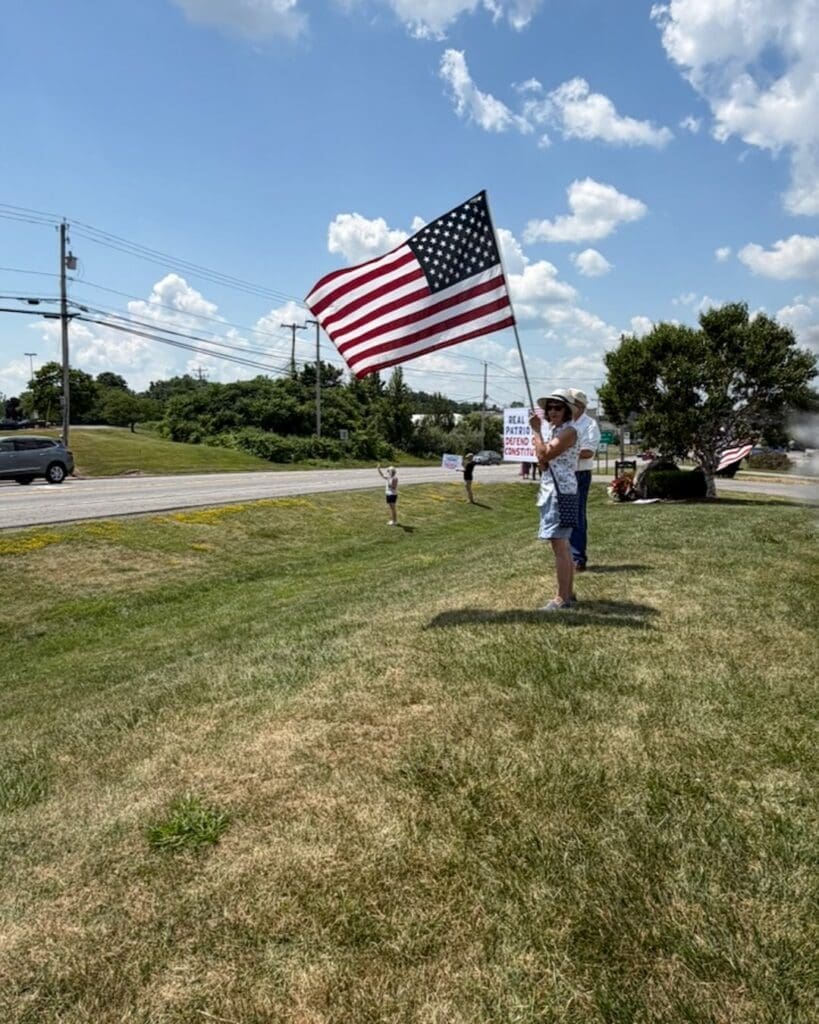 People holding American flag at roadside protest on sunny day