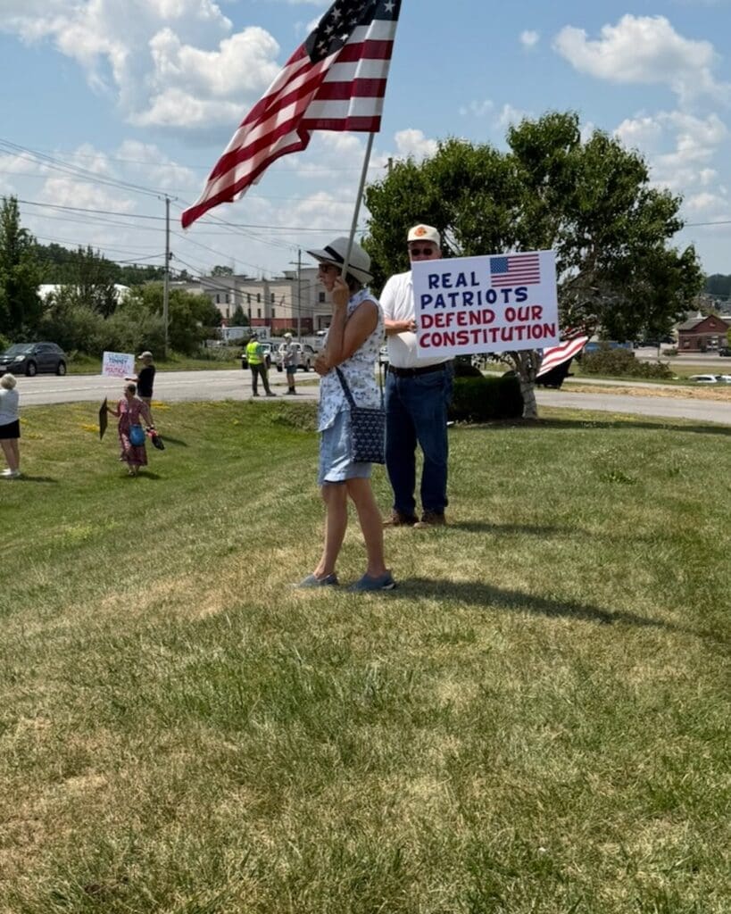 Protesters holding American flag and Constitution defense sign outdoors