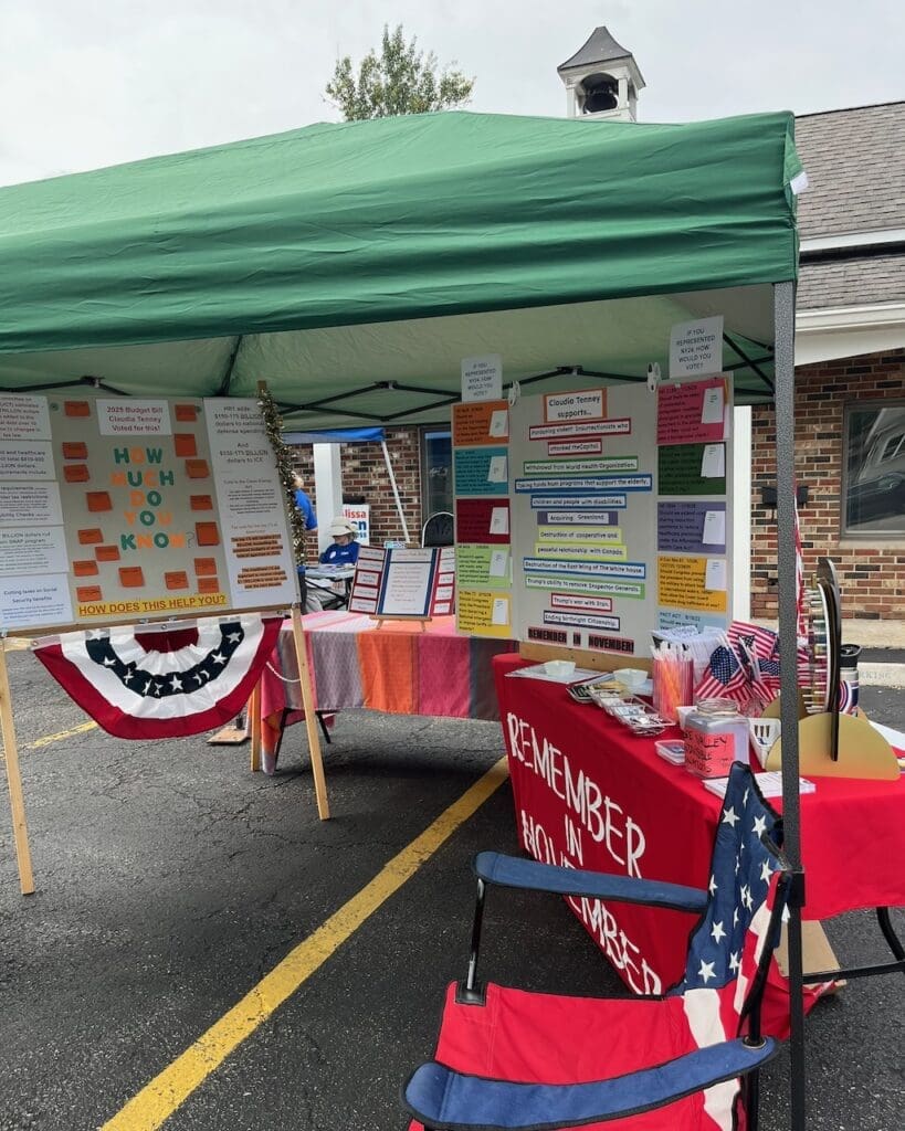 Political information booth with signs under green canopy outdoors