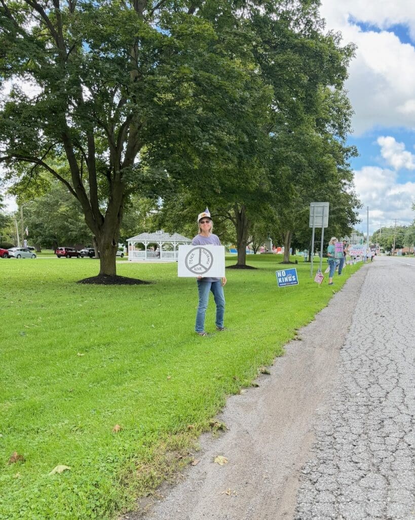 Person holding peace sign protest sign along roadside park