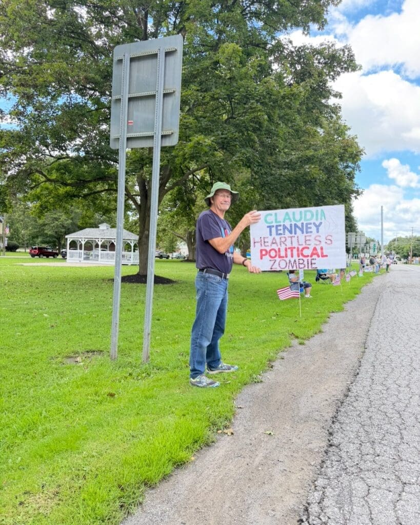 Man holding protest sign against Claudia Tenney roadside